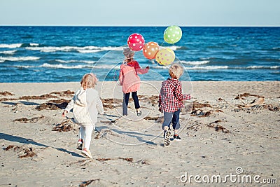 Group portrait of funny white Caucasian children kids with colorful bunch of balloons, playing running on beach on sunset Stock Photo