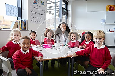 Group portrait of infant school teacher and kids sitting at table in a classroom looking to camera smiling, front view Stock Photo