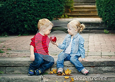 Group portrait of two white Caucasian cute adorable funny children toddlers sitting together sharing apple food Stock Photo