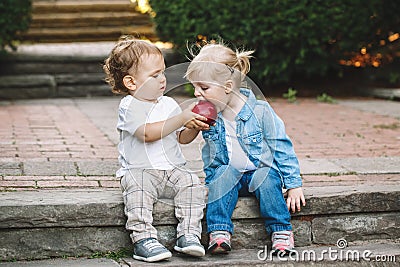 Two white Caucasian cute adorable funny children toddlers sitting together sharing eating apple food Stock Photo