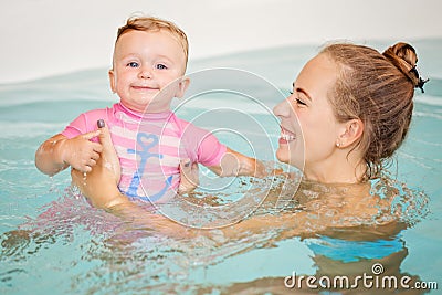 Group portrait of white Caucasian mother and baby daughter playing in water diving in swimming pool inside, looking in camera Stock Photo