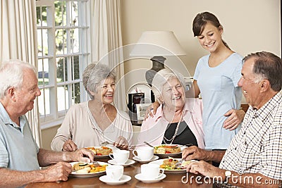 Group Of Senior Couples Enjoying Meal Together In Care Home With Teenage Helper Stock Photo