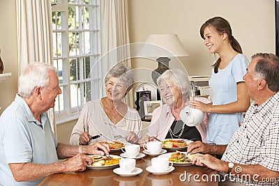 Group Of Senior Couples Enjoying Meal Together In Care Home With Teenage Helper Stock Photo