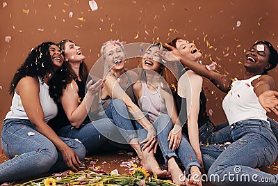 Group of six laughing women of different ages sitting under falling flower petals. Multi-ethnic smiling females having fun in Stock Photo