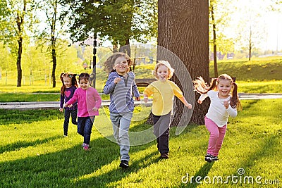 A group of small happy children run through the park in the background of grass and trees. Stock Photo