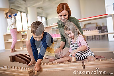 Group of small nursery school children with teacher sitting on floor indoors in classroom, montessori learning. Stock Photo