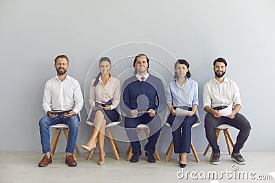 Smiling candidates job seekers sitting in row with resumes in hand and waiting for interview invitation turn Stock Photo