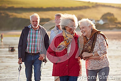 Group Of Smiling Senior Friends Walking Arm In Arm Along Shoreline Of Winter Beach Stock Photo