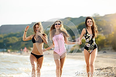 Group of three beautiful attractive young women running on the beach near the sea shore and splash watter dropplets and Stock Photo