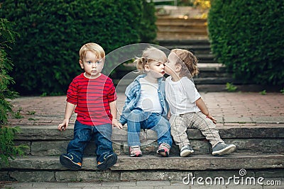 Group of three cute funny adorable white Caucasian children toddlers boys girl sitting together kissing each other Stock Photo