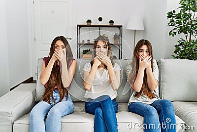 Group of three hispanic girls sitting on the sofa at home shocked covering mouth with hands for mistake Stock Photo