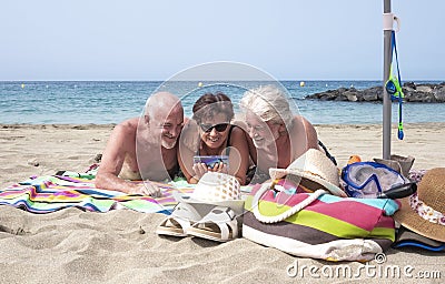Group of three people friends mature and senior hugging enjoying together holidays at the beach having fun with smart phone - Stock Photo