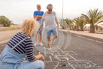 Group of three people like adults and senior - two seniors playing at hopscotch with a curly woman looking at the mature woman Stock Photo