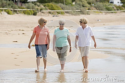 Group of three senior mature retired women on their 60s having fun enjoying together happy walking on the beach smiling playful Stock Photo