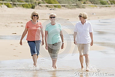 Group of three senior mature retired women on their 60s having fun enjoying together happy walking on the beach smiling playful Stock Photo