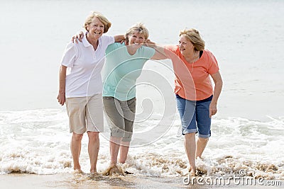 Group of three senior mature retired women on their 60s having fun enjoying together happy walking on the beach smiling playful Stock Photo