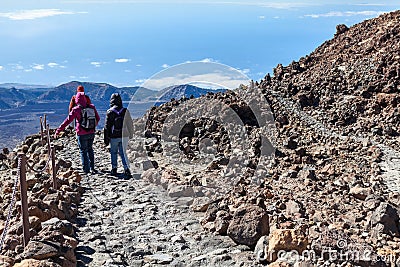 A group of tourists descend from the summit of the Teide volcano along a stone staircase among the lava heap. Three people in Stock Photo