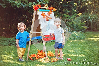 Group of two white Caucasian toddler children kids boy and girl standing outside in summer autumn park by drawing easel Stock Photo