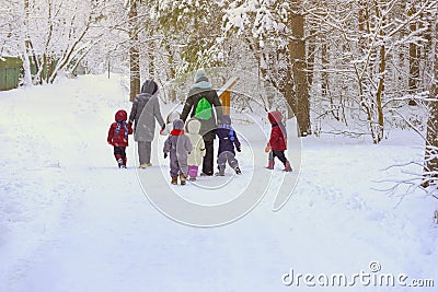 Group of unrecognizable litle kids with teachers of kindergarten, back to us, walk holding hands in snowy park, winter Editorial Stock Photo