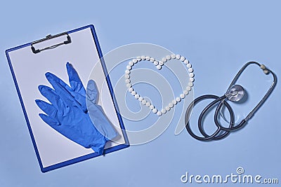 Group of white round pills forms heart figure from white pills, notebook, blue gloves and stethoscopen on blue Stock Photo