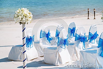 A group of white spandex chairs cover with blue organza sash for beach wedding venue setup Stock Photo