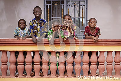 Group of Young African Children Linung Up On Their City Home Balcony Smiling to Bypassers Stock Photo
