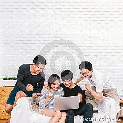 Group of young Asian people cheering together using laptop computer at home with copy space. Success teamwork, friends activity Stock Photo