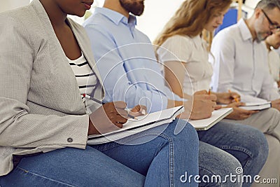 Group of young business people sitting on chairs in a row and writing in notebooks. Stock Photo