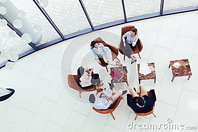 Group of young business professionals sitting together and having casual discussing in office hallway achieving goals. Stock Photo