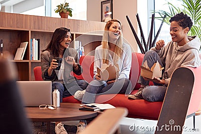 Group Of Young Businesswomen Sitting On Sofas In Open Plan Workspace Having Working Lunch Meeting Stock Photo