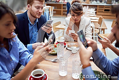 Group of young caucasian people having unsocial lunch in restaurant, using their cell phones and not talking to each other. Stock Photo