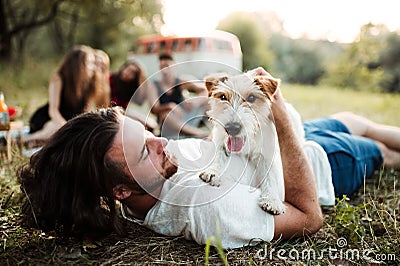 A group of young friends with a dog sitting on grass on a roadtrip through countryside. Stock Photo