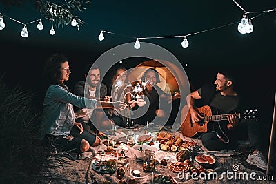 Group of young happy friends having picnic outdoors with sparklers Stock Photo