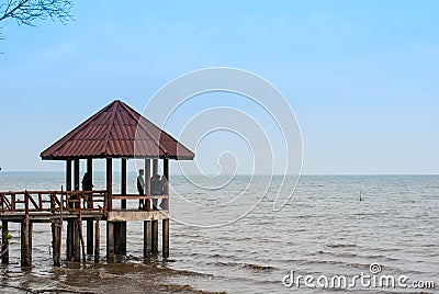 A group of young men and women hanging out in the red old pavlion on the beach reaching into the sea with blue sky, relaxing day Editorial Stock Photo