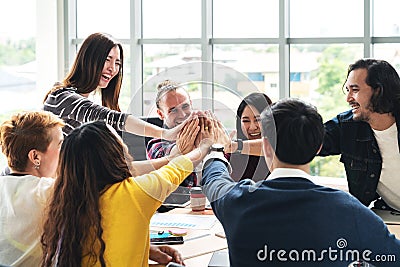 Group of young multiethnic diverse people gesture hand high five, laughing and smiling together in brainstorm meeting at office. Stock Photo