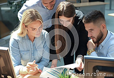 Group of young people in casual wear sitting at the office desk and discussing something while looking at PC together. Stock Photo