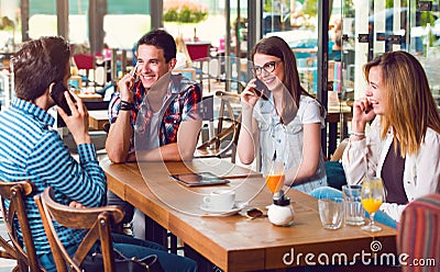 Group of young people sitting at a cafe, talking over phones Stock Photo