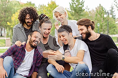 A group of young people are working in the park with mobile phones.They all laugh looking at the phone Stock Photo