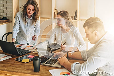 Group of young people working together. Man is using laptop, girls looking on screen of laptop, discussing business plan Stock Photo