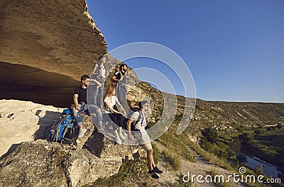 Group of young smiling tourists hikers having rest on natural rocks and enjoying green valley landscape Stock Photo