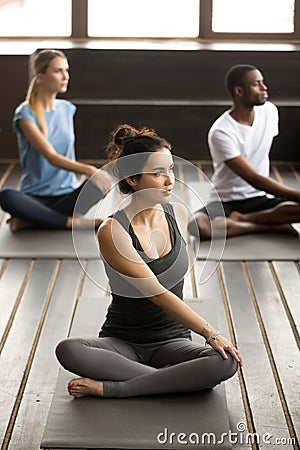 Group of young sporty people sitting in parivritta sukhasana pos Stock Photo