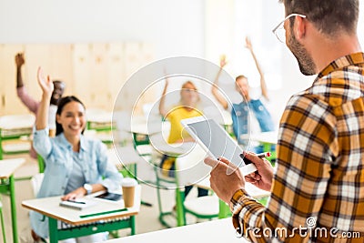 group of young students raising up hands to answer on teachers question while he standing with tablet Stock Photo