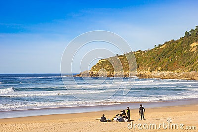 Group of young surfers sitting on the Zurriola beach of San Sebastian Editorial Stock Photo