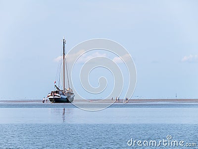 Group of youngsters on sand flat and flat-bottom sailboat at low Editorial Stock Photo