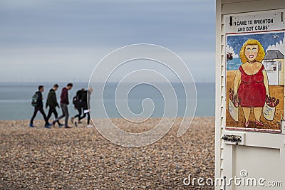 Group of youths walking along brighton beach with saucy seaside image Editorial Stock Photo