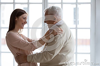 Grownup granddaughter visited elderly grandfather hugs him standing indoors Stock Photo