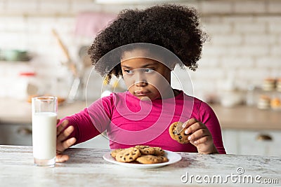 Grumpy Little Black Girl Refusing Milk And Eating Cookies In Kitchen Stock Photo