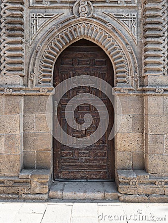 Grunge wooden ornate aged vaulted arched door on exterior decorated stone bricks Stock Photo