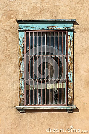 Grungy barred window on stucco wall with peeling turquoise paint Stock Photo