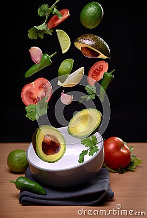 Guacamole ingredients flying over bowl on black solid background. tomato, pepper, onion, garlic, avocado, coriander, lime Stock Photo